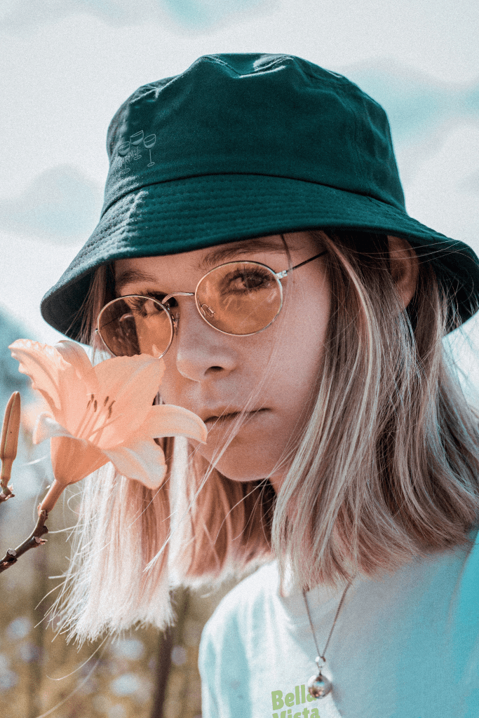Girl smelling a flower, while wearing glasses and a bucket hat with Bella Vista Wine Society logo